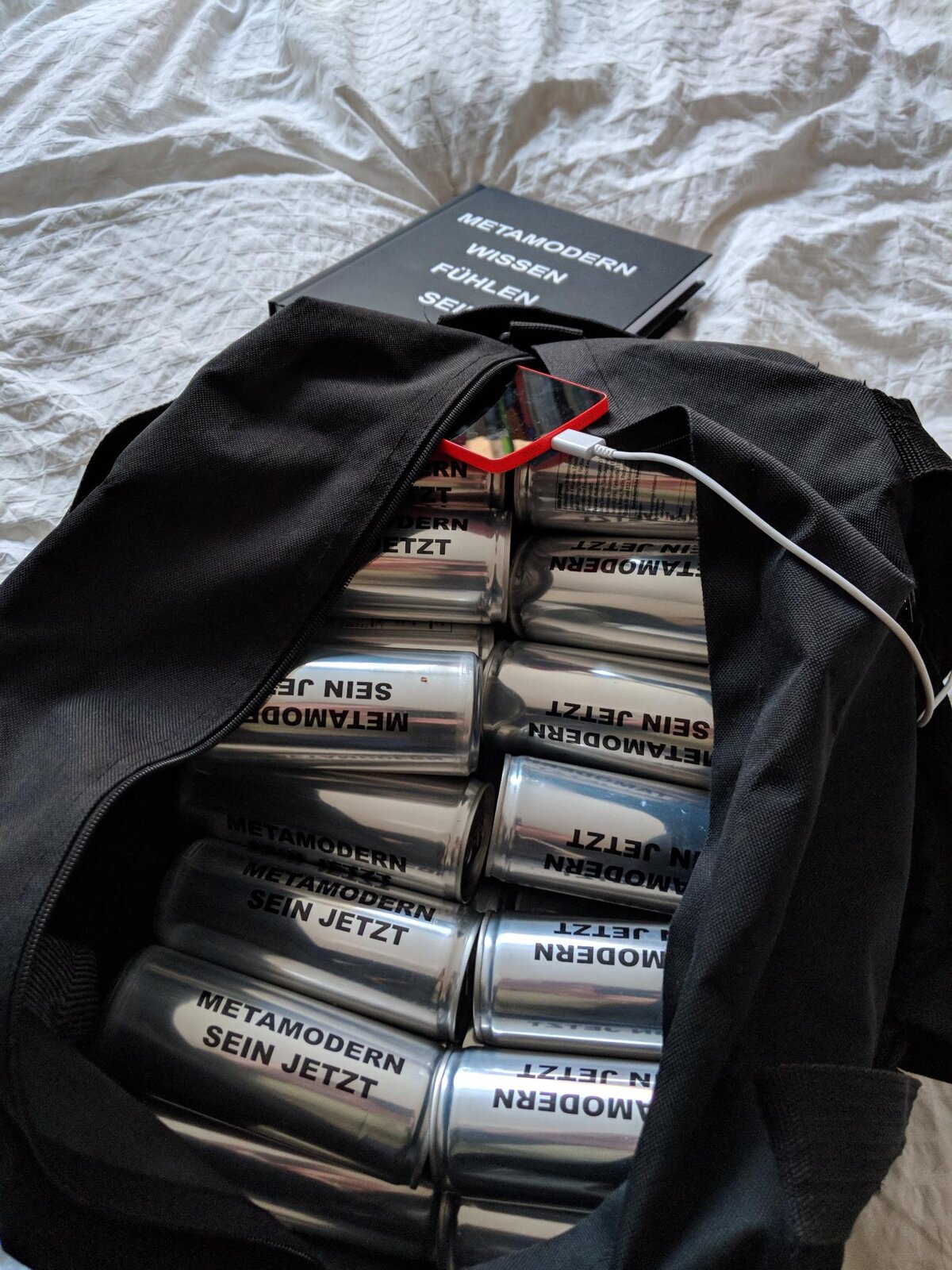 'METAMODERN SEIN JETZT' cans packed into a bag next to a copy of METAMODERN WISSEN FÜHLEN SEIN, before departure to Nürnberg