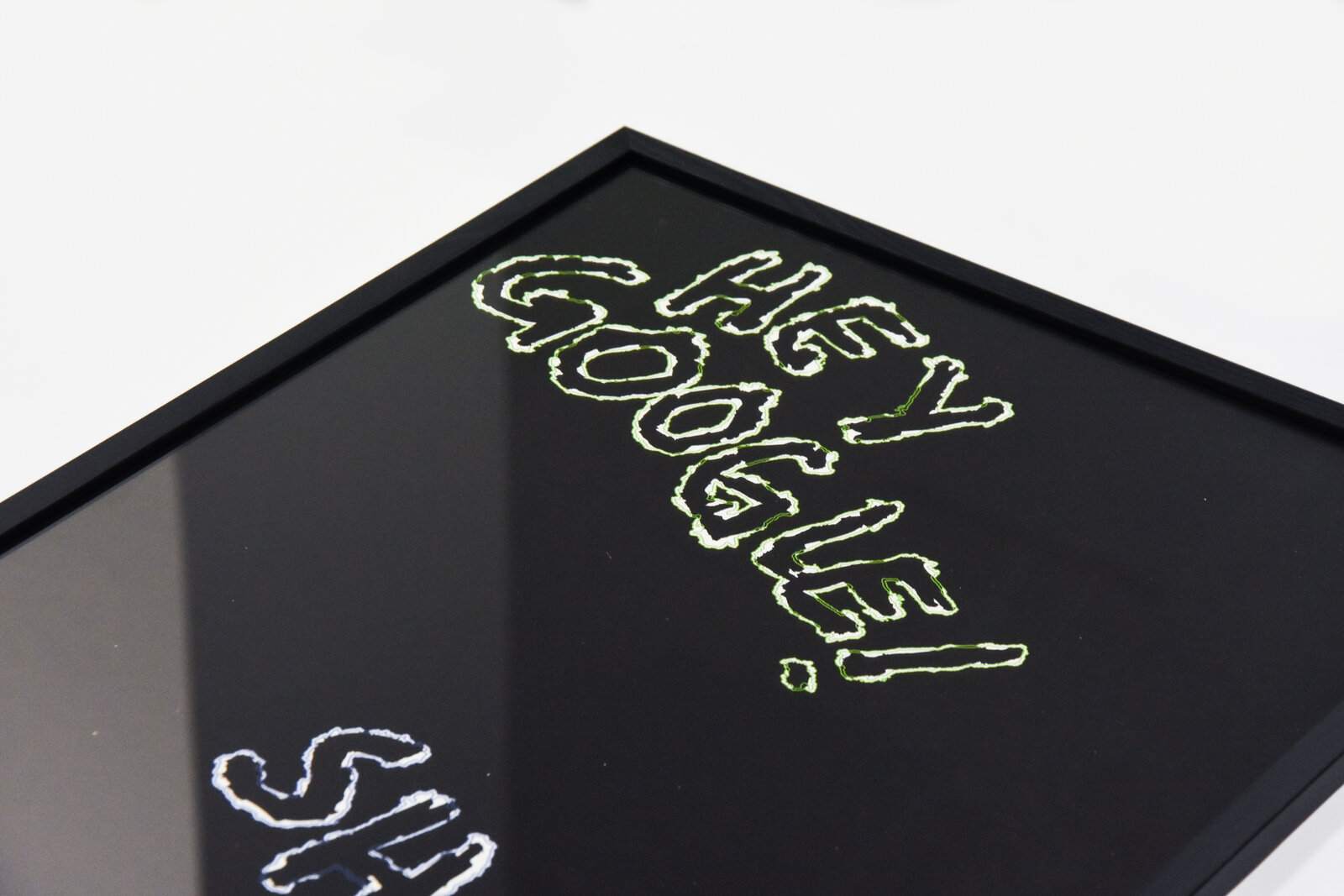 Detail of the framed print: 'HEY GOOGLE!' corner, glossy reflection across the glass