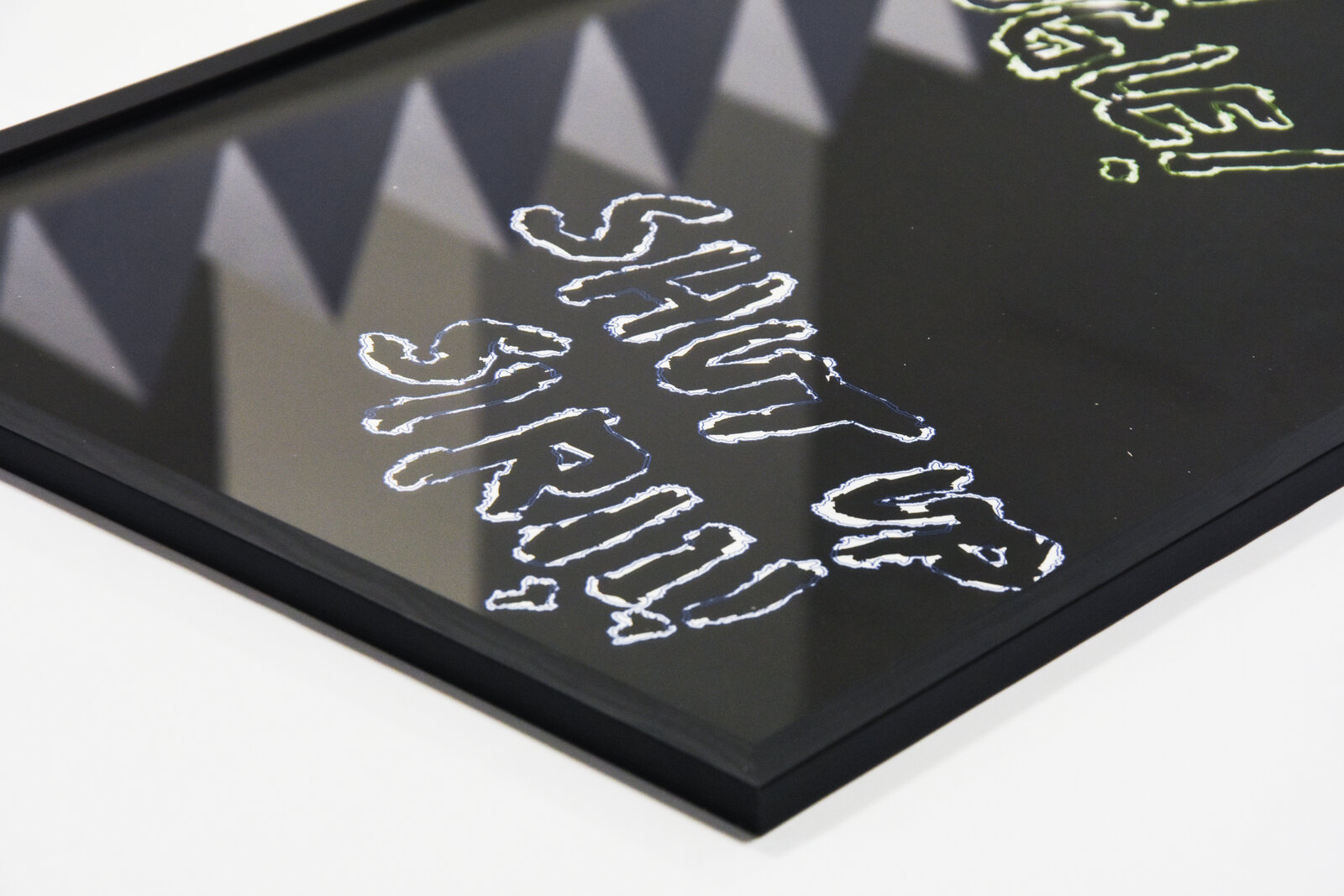 Detail of the framed print: 'SHUT UP SIRI!!!' corner, foam wall panels reflected in the glass