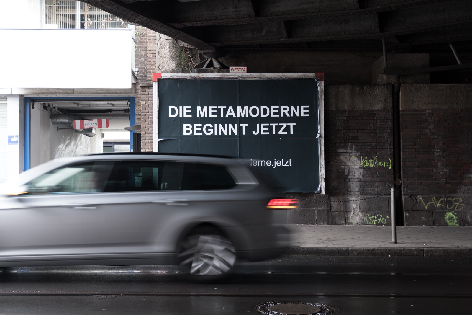 The same poster by day, a car passing in motion blur
