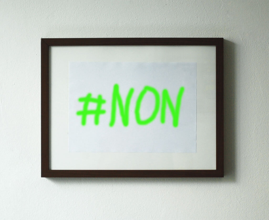 A framed sheet of paper with '#NON' handwritten in green marker