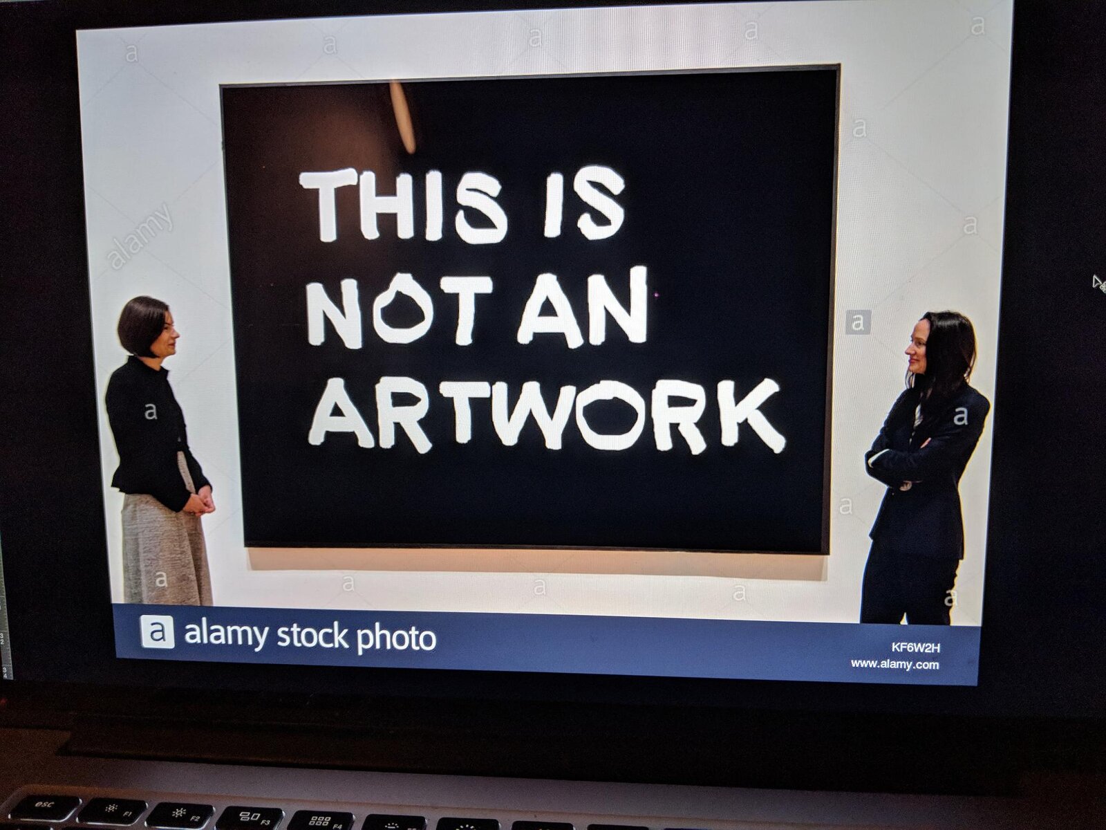 A gallery wall reading 'THIS IS NOT AN ARTWORK', two visitors looking at it from either side