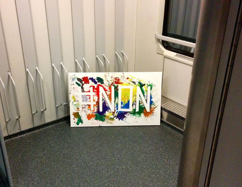 A painting reading '#NON' in scrawled colour, propped on a regional train