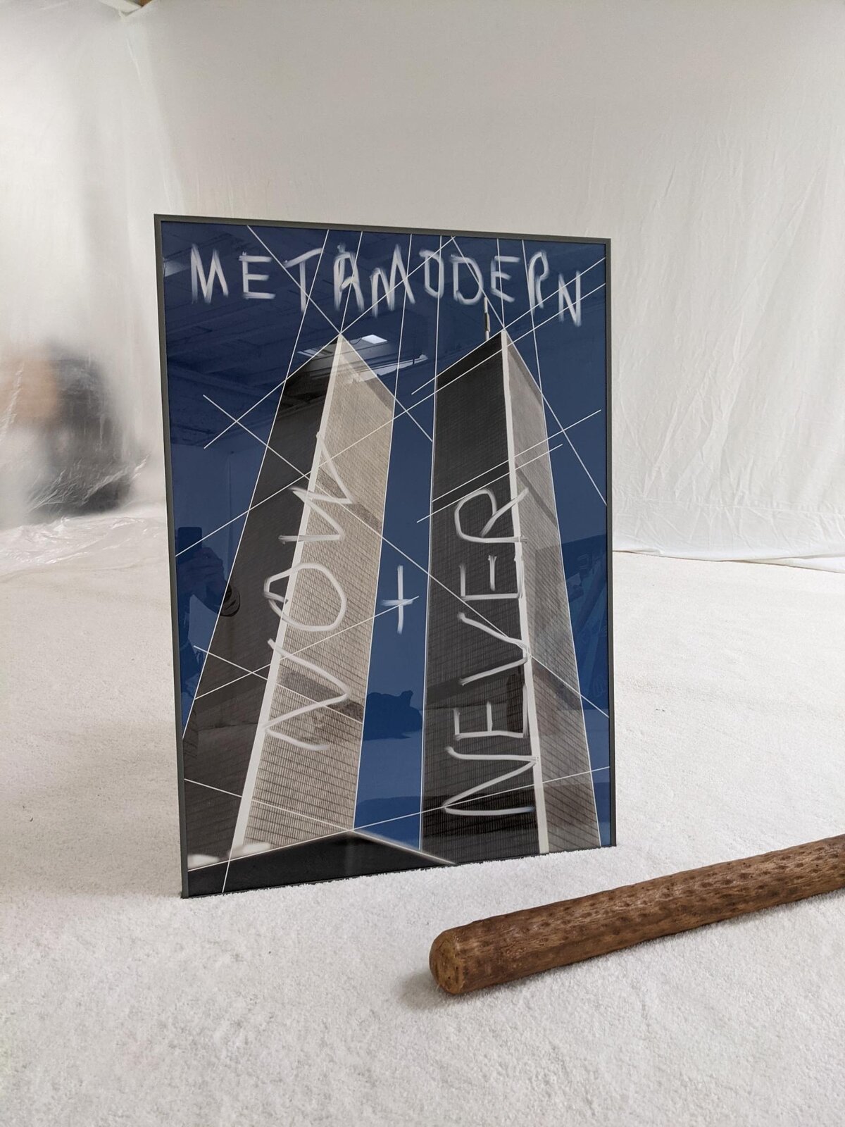 A framed print of the Twin Towers with 'METAMODERN NOW + NEVER' scrawled across it, propped against a white backdrop