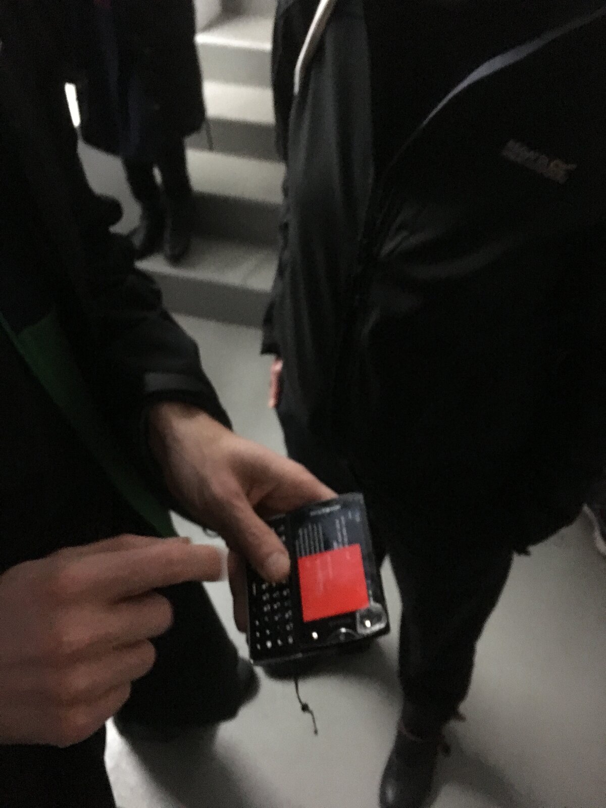 A phone with a red screen held out at the Berlin vernissage, people in dark winter coats on a stairwell in the background