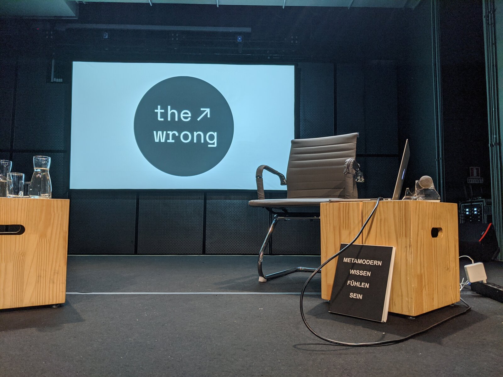 A stage set for 'the wrong' biennale, a copy of METAMODERN WISSEN FÜHLEN SEIN resting on a wooden crate in front of the lectern